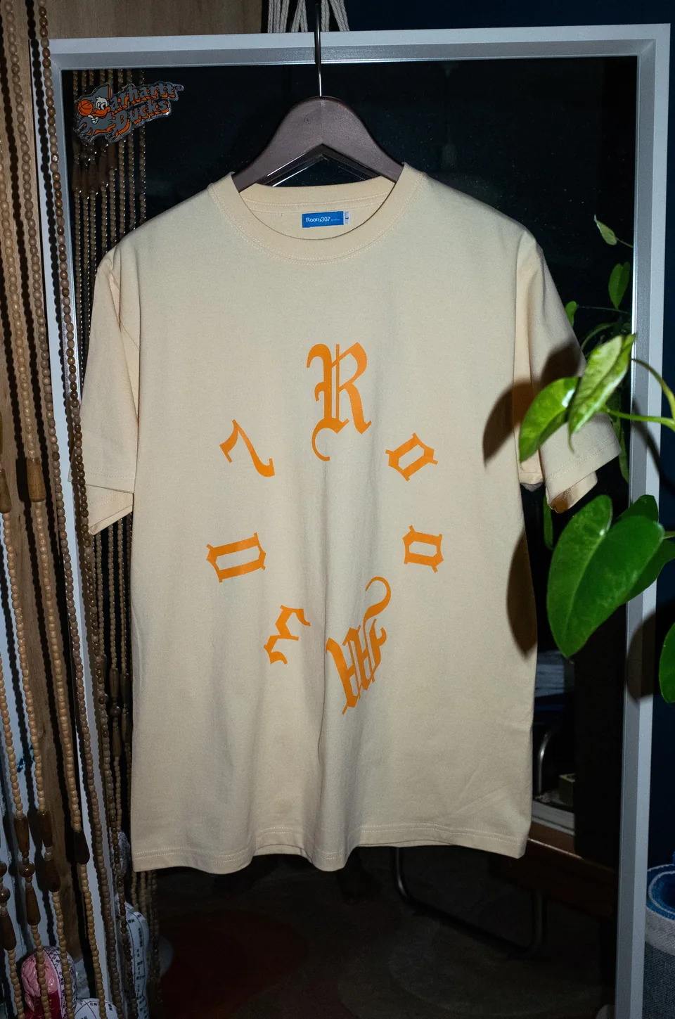 Model wearing the apricot and orange Room307 logo T-shirt.